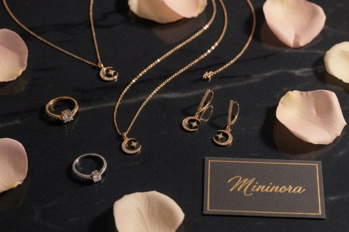 Gold jewelry set including necklaces, rings, and earrings on a dark surface with pink petals around, featuring the brand 'Mininora'.