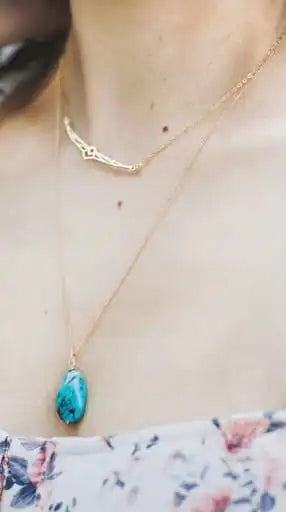 Necklace with a turquoise pendant worn by a person with floral clothing.